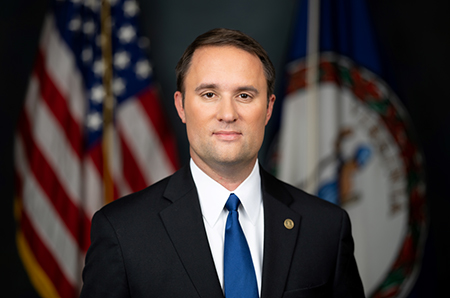 Photograph of Attorney General Jason Miyares in front of the US Flag and the VA State Flag